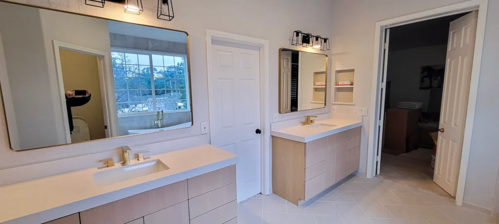 Modern double vanity bathroom remodel in Pleasanton CA featuring light wood cabinets, white quartz countertops, and gold fixtures by Lions Gate Remodeling.