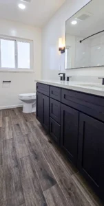 Modern bathroom remodel in Oakland, CA featuring dark vanity, white walls, and wood-look tile flooring