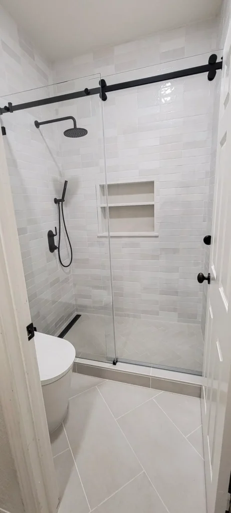 Guest bathroom remodel in Pleasanton CA featuring modern glass shower enclosure, white subway tile, built-in niche shelving, and matte black fixtures by Lions Gate Remodeling.