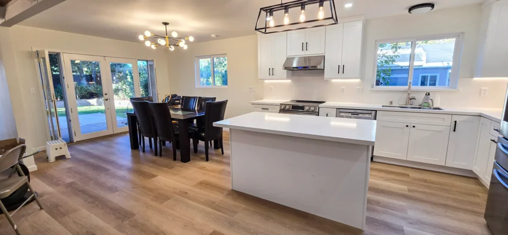 Open concept kitchen and dining remodel in Santa Clara with white shaker cabinets, quartz island, wood flooring and backyard access by Lions Gate Remodeling