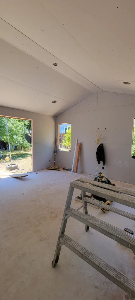 Interior drywall stage of a master bedroom addition in Martinez California showing vaulted ceiling and new windows during construction