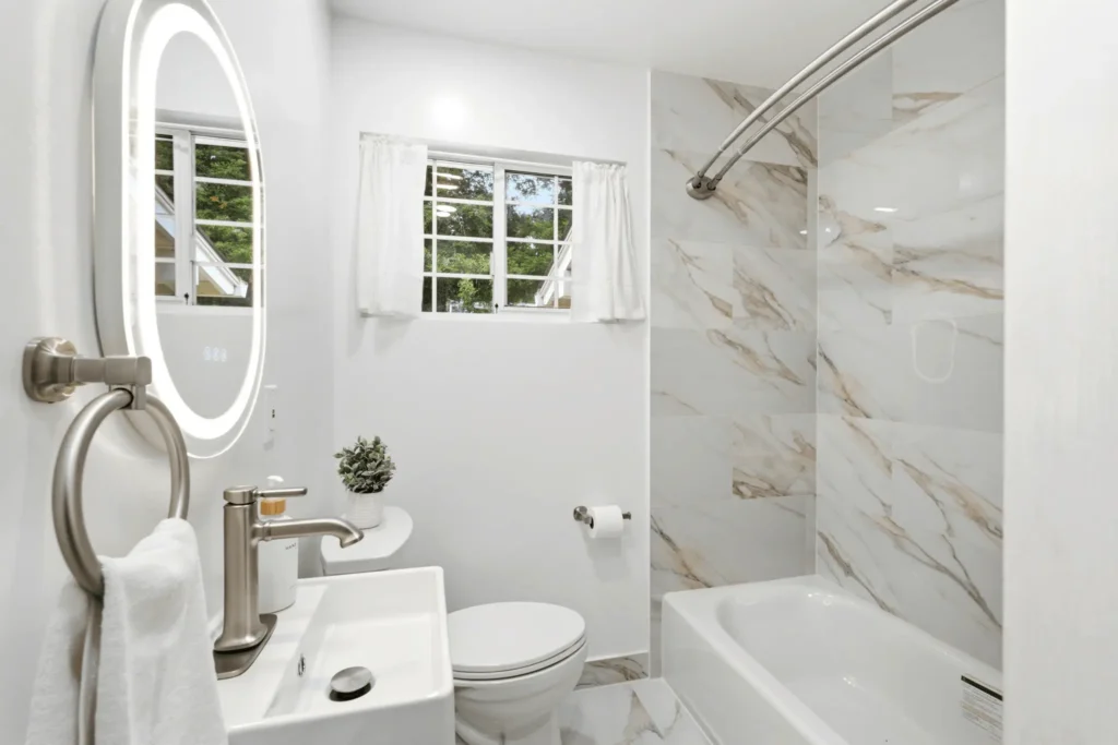 Completed bathroom remodel featuring a floating vanity, LED mirror, and marble-look tile.